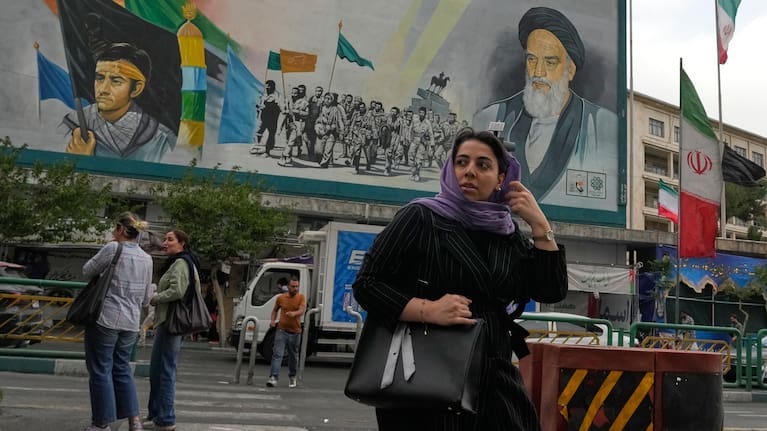 A woman crosses a street in front of a painting of the late Iranian revolutionary founder Ayatollah Khomeini and paramilitary Basij forces in downtown Tehran, Iran, Sunday, May 24, 2026.