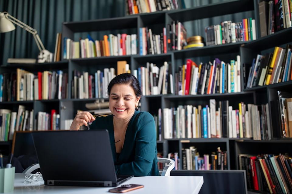 Person smiling while sitting on a desk and reading on a laptop in a library. 