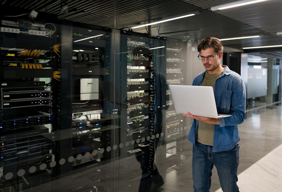 A person holding a laptop walks through a data center. 