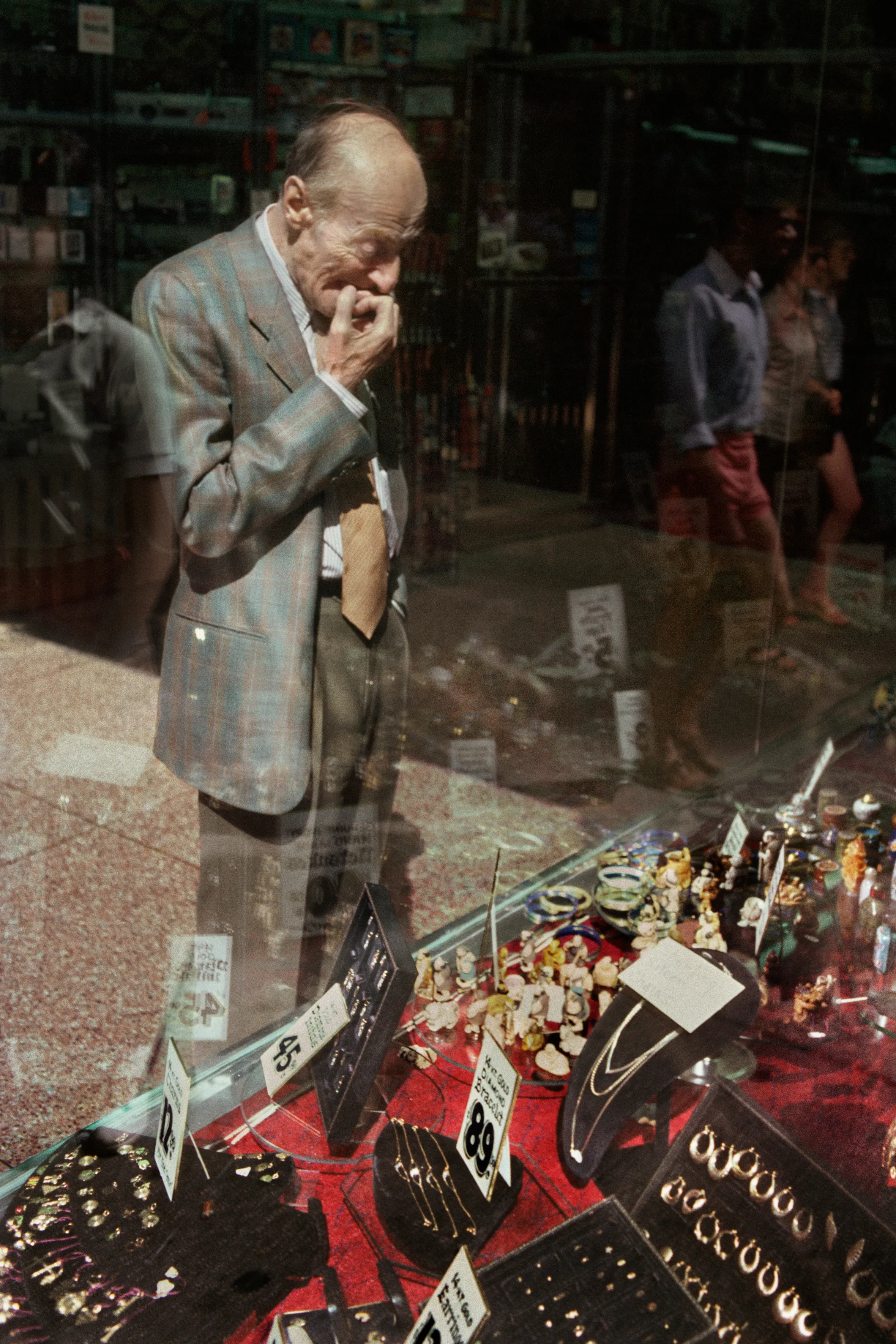 Elderly man in a plaid suit looking at jewelry in a Manhattan shop window.