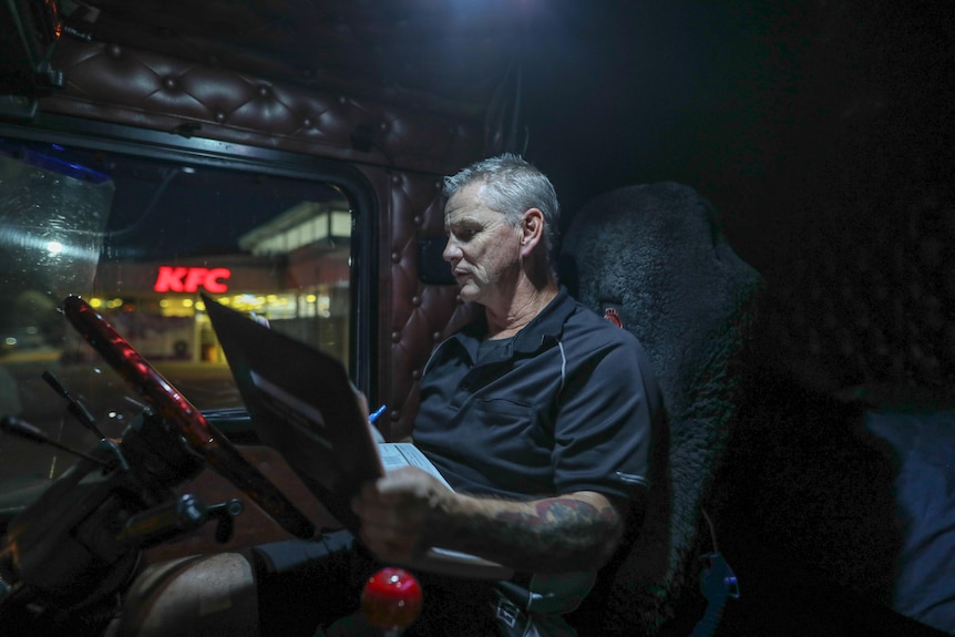 Sean Mulvaney sits in the cab of his truck at night and writes in a log book balanaced 