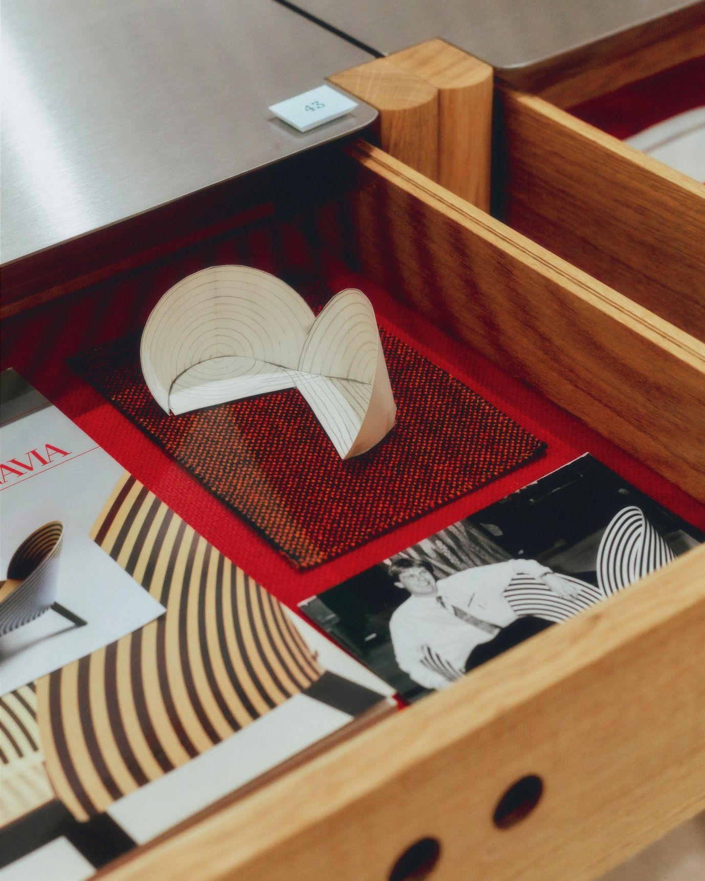 A wooden drawer filled with design memorabilia in red, black and white, and yellowed paper.