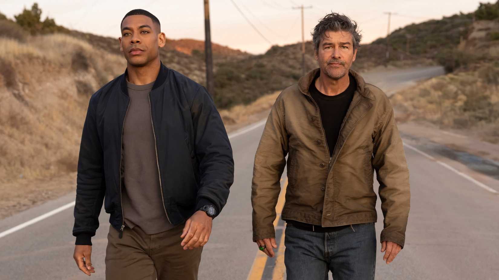 Aaron Pierre and Kyle Chandler walking down a road in Lanterns