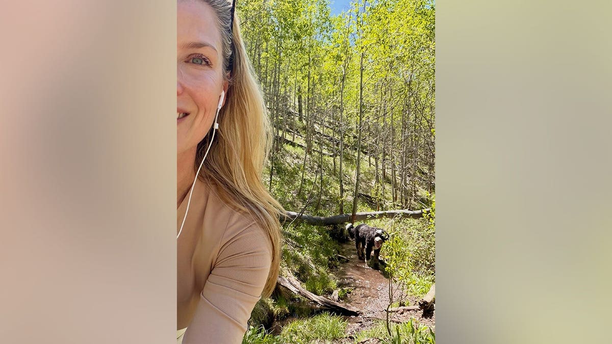 Ali Larter smiling at the camera while hiking with her dog behind her in May 2026.
