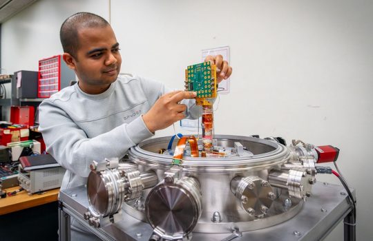 Fermilab engineer Yash Saxena holds a custom circuit board designed to measure chip performance in cryogenic environments. Credit: JJ Starr, Fermilab