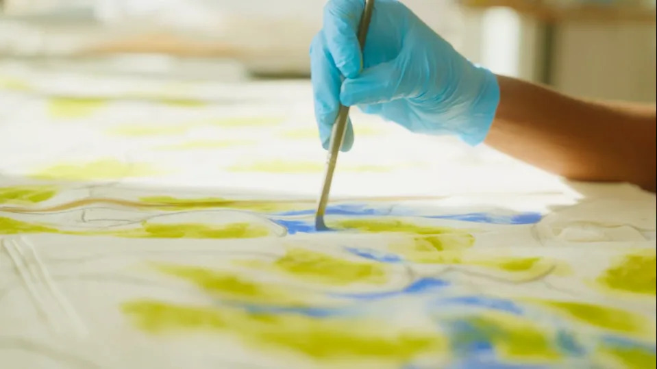 Hand painting with a brush on fabric using blue and green colors.