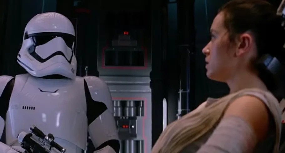 A stormtrooper holds a blaster while a woman is seated, in a scene from a sci-fi movie