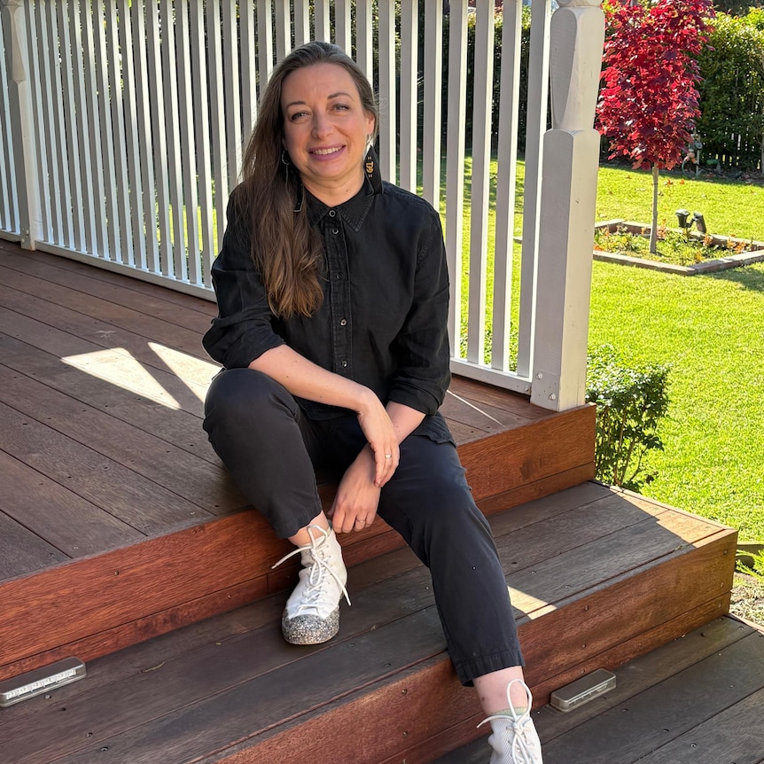 A woman sitting on a deck smiling for the camera