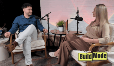 Two people seated in armchairs during a podcast interview, speaking into microphones across a small table with water glasses and a plant, with a “TechCrunch Build Mode” logo overlay in the corner.