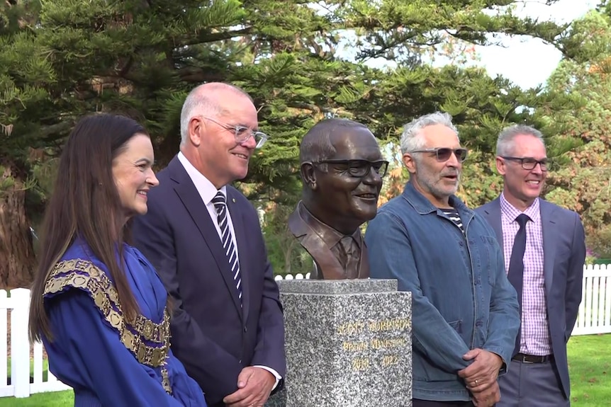 Scott Morrison, and three other people, standing next to a bronze bust of Mr Morrison.