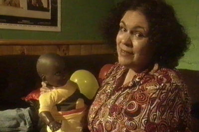 A woman holds a doll wearing a T-shirt with the Aboriginal flag.