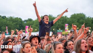 Festivalgoers enjoy a performance during BBC Radio 1's Big Weekend. There are fans in the crowd who are singing along and one who is raised up with his arms in the air.