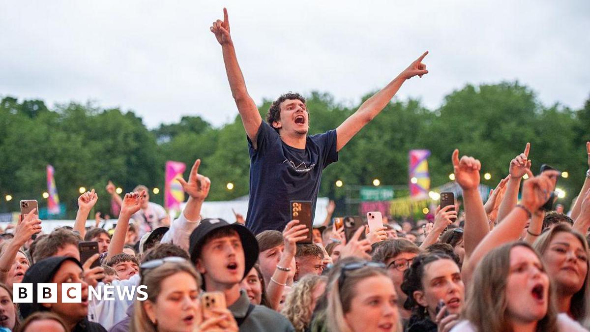Festivalgoers enjoy a performance during BBC Radio 1's Big Weekend. There are fans in the crowd who are singing along and one who is raised up with his arms in the air.