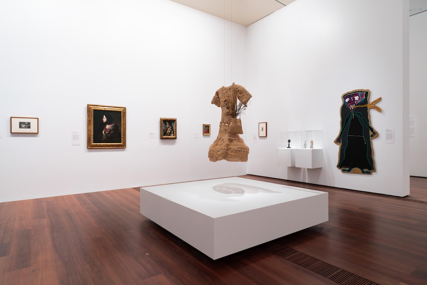 A gallery room with framed and unframed portraits on the walls and a woven torso in the centre.