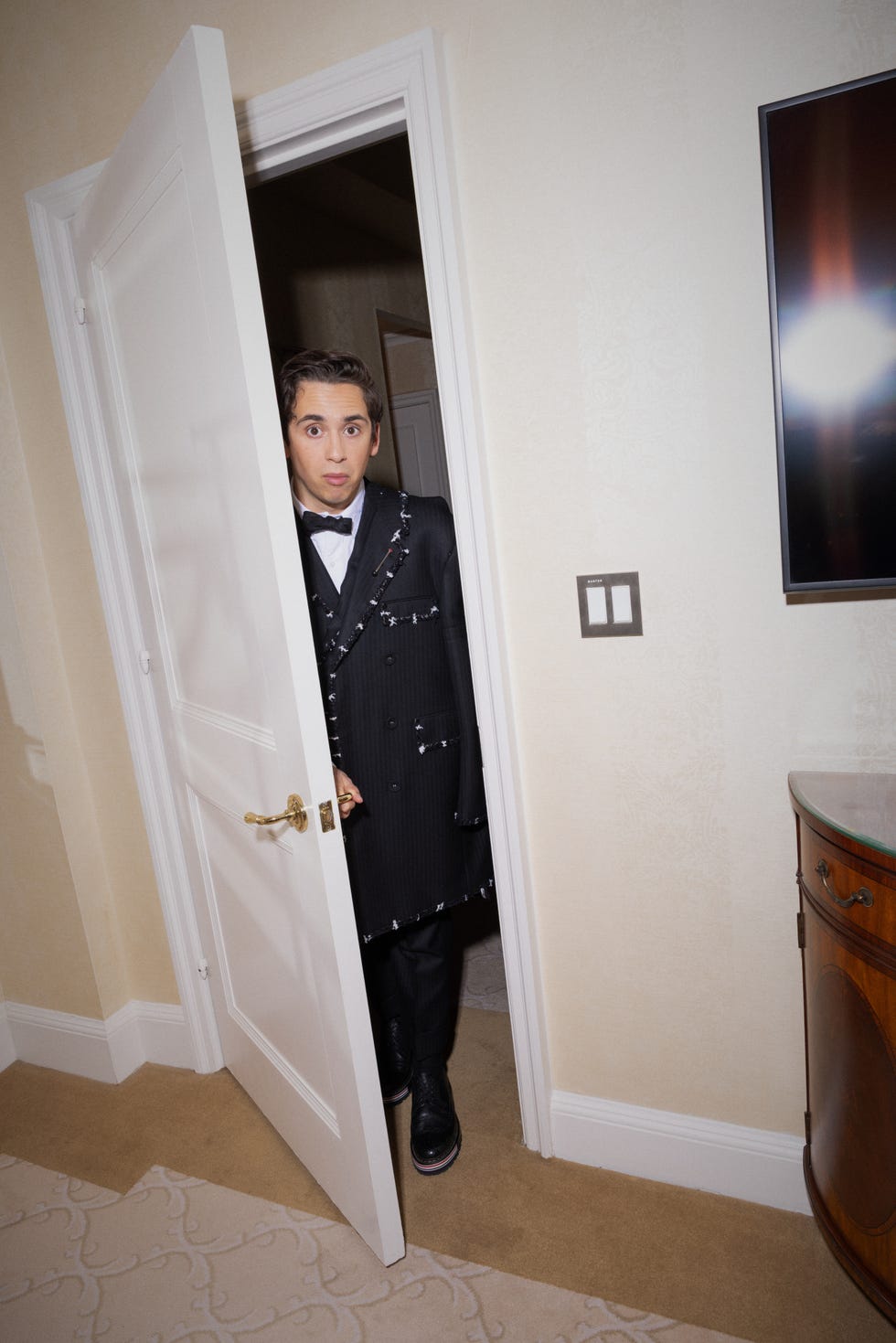 A person in a formal outfit stands at a partially open door.