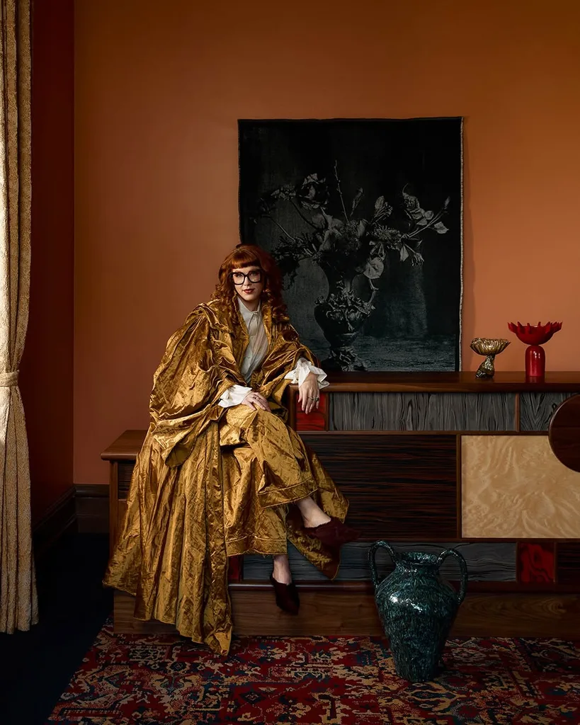 A woman sitting in a gold cape in a room painted orange