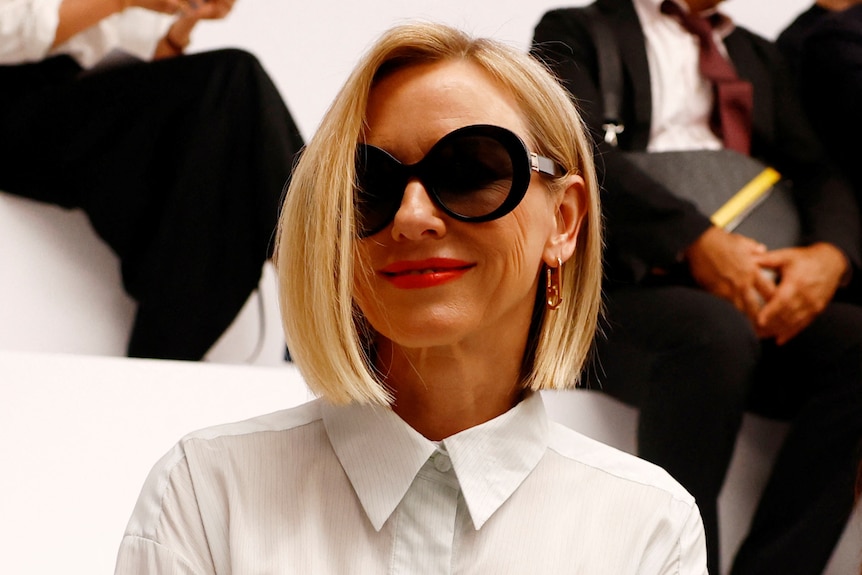 Naomi Watts wearing a white shirt and sunglasses with short blonde hair