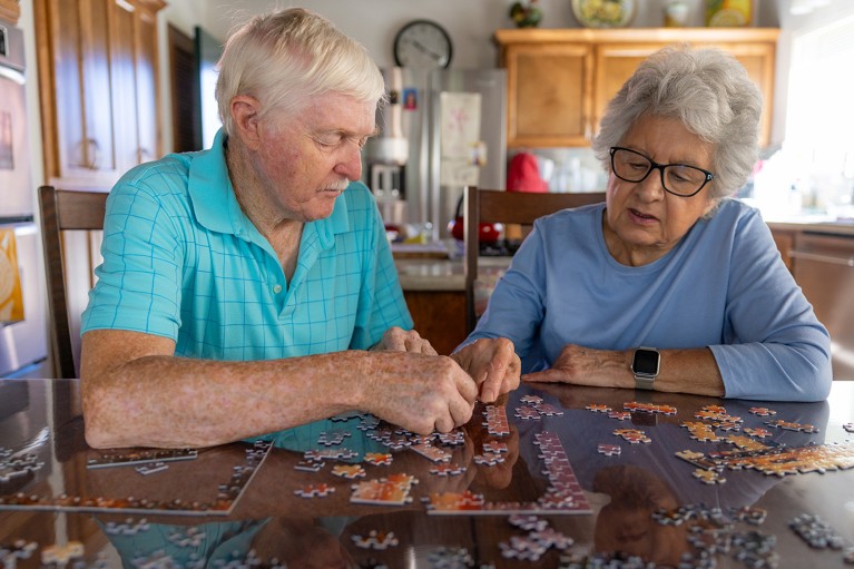 An older couple sitting at a table doing a jigsaw puzzle.