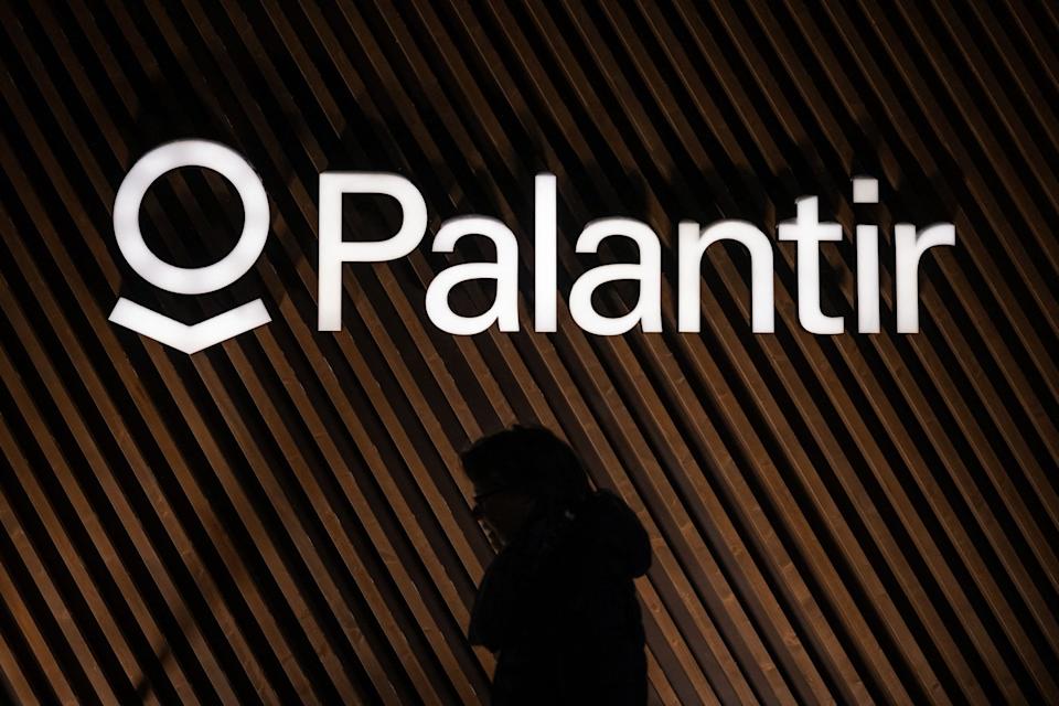 A shadowy figure walking past the Palantir logo on a wall.