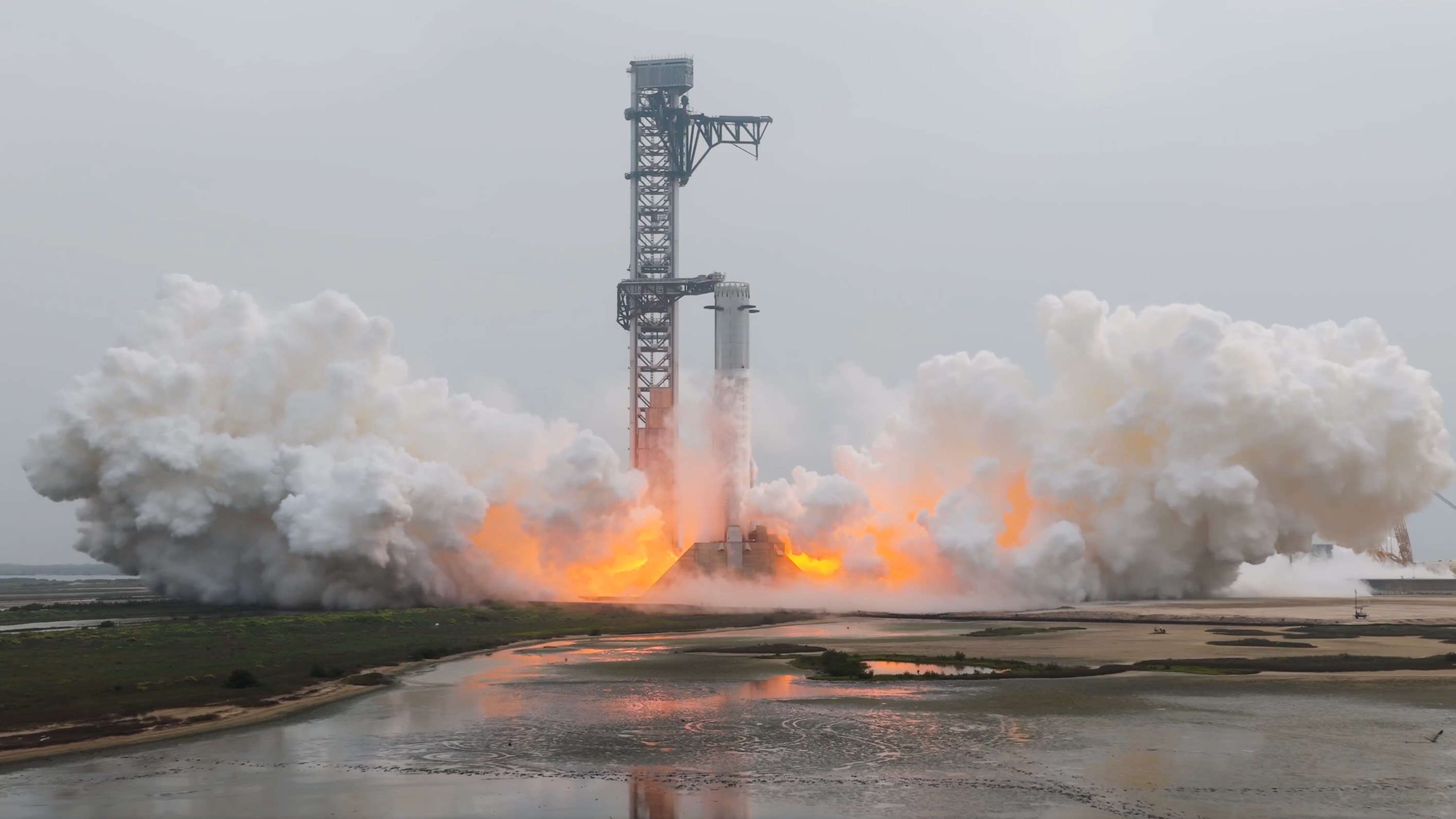 side view of a silver rocket firing its engines on the launch pad during a test