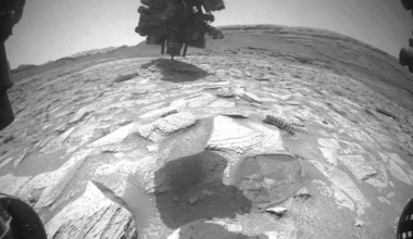 Looped video footage of a slab of rock stuck to the robotic arm of the Curiosity rover as the arm moves and rotates to remove it