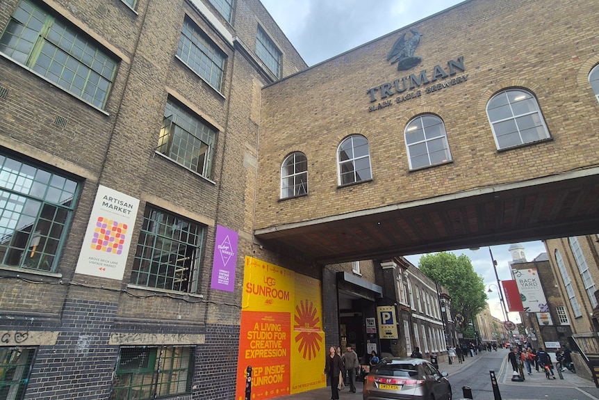 A large building with the Truman Brewery logo on it, spanning over a narrow London street.