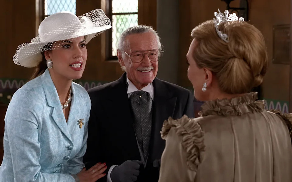 Three people in elegant attire at a formal event, engaged in conversation, with hats and a bow tie featured prominently