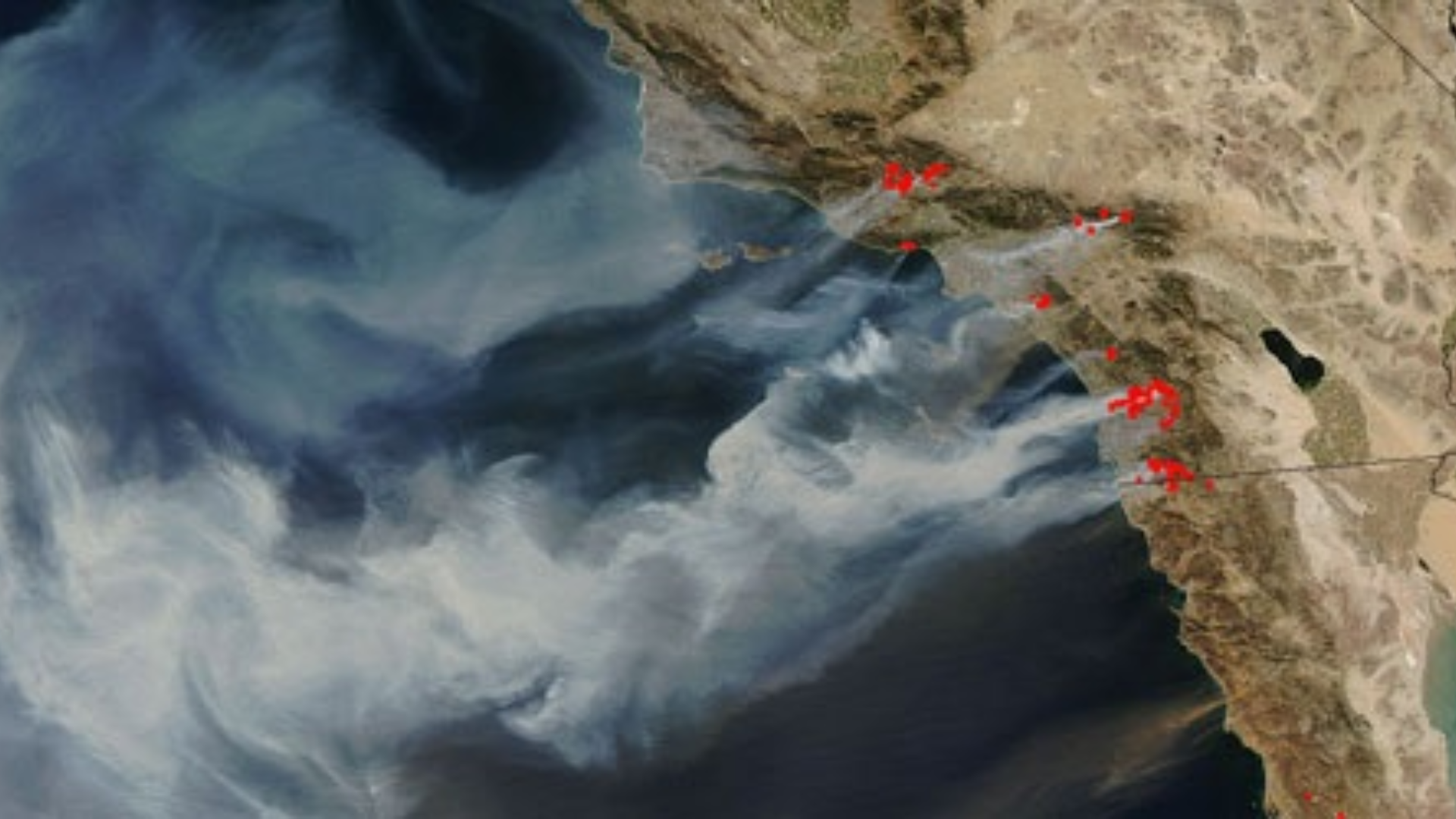 A view from a satellite of a coastline. White smoke blows off the coast.