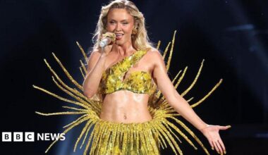 Zara Larsson wearing a yellow sparkly two piece outfit. She has long blonde hair and she is singing into a microphone.
