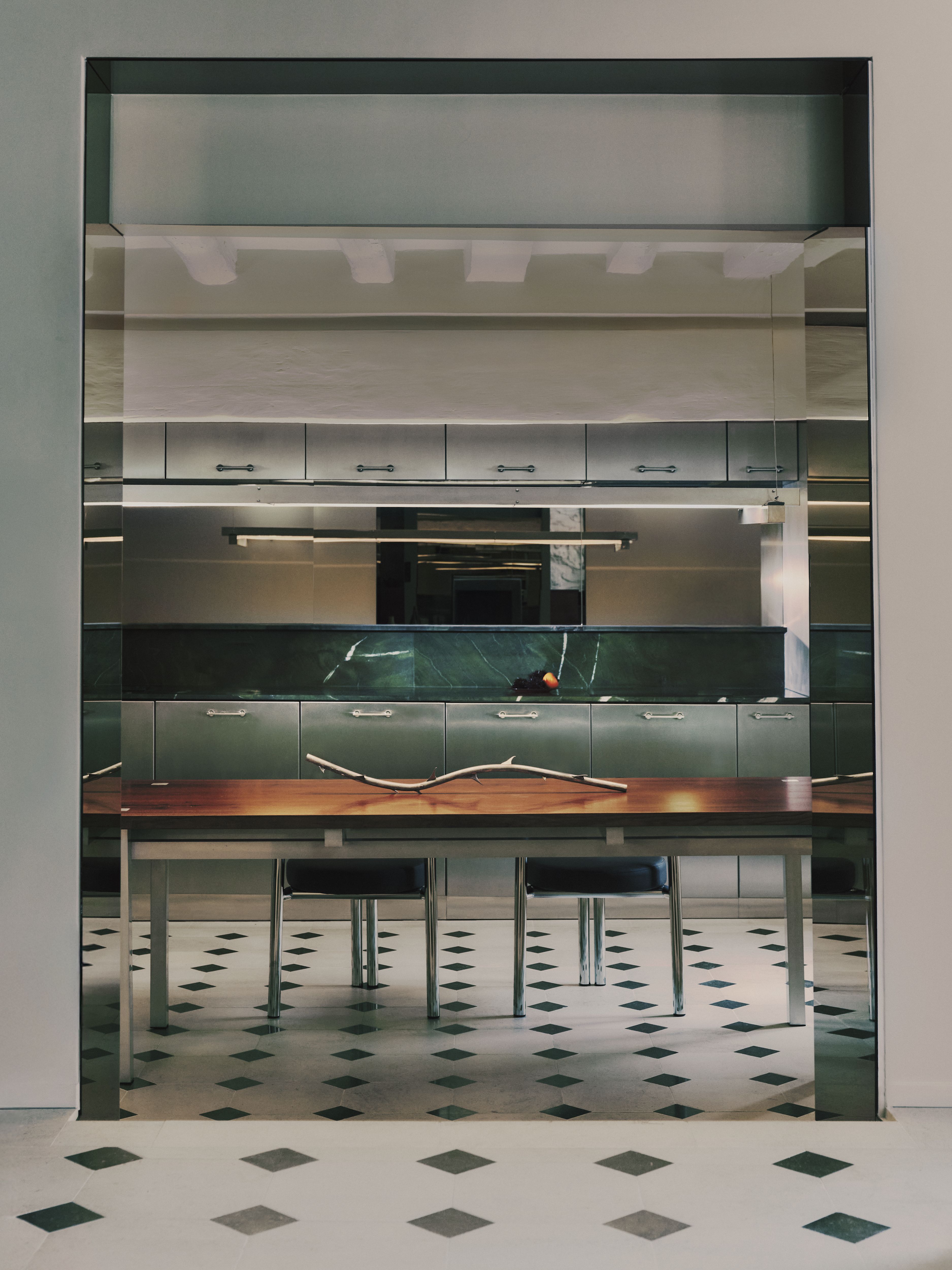 A sleekly designed apartment with tiled white and black checkered floors, chrome surfaces, brick walls, and occasional pops of red, ming green, and butter across linearly cut furniture.