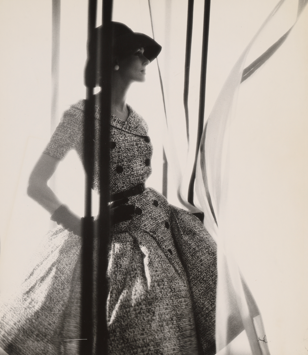 Fashion model posing in a vintage dress with a hat, framed by flowing fabric.