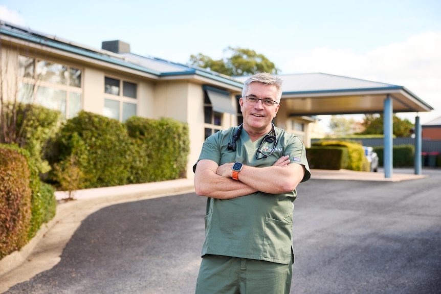 A man in doctor's scrubs stands outside a facility.
