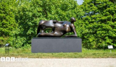 Henry Moore's statue Reclining Woman: Elbow on a patch of grass next to a path.