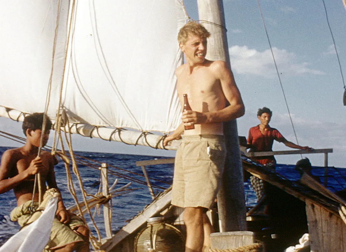 David Attenborough on a boat holding a bottle, with two other men.