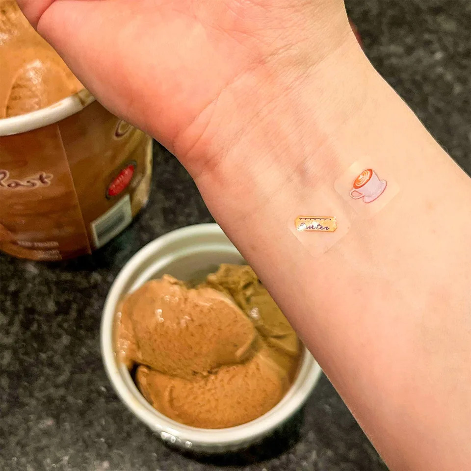 Hand with decorative stickers next to bowls of ice cream.