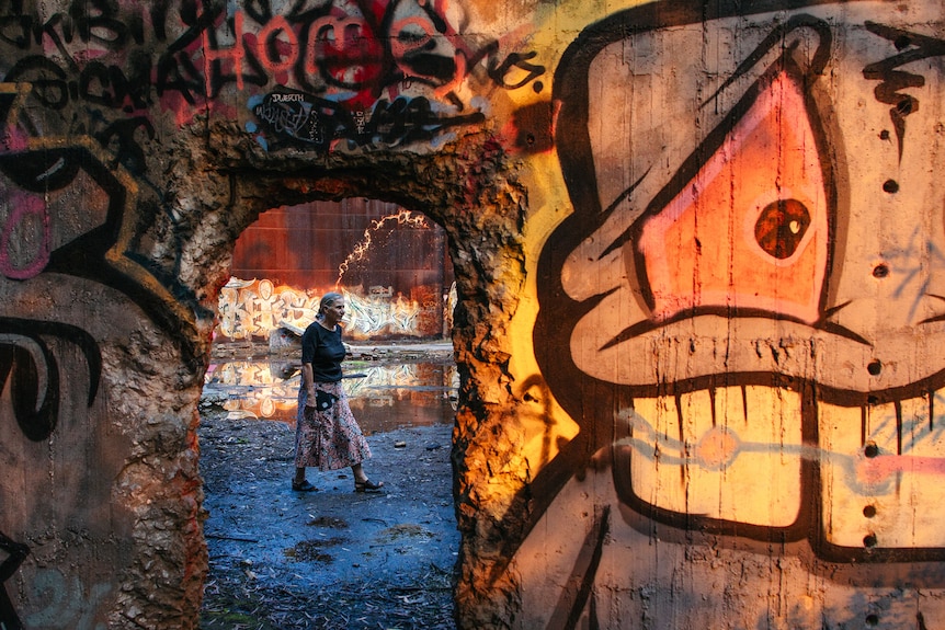 A woman walks along the floor of a huge concrete storage tank that is covered in graffiti.