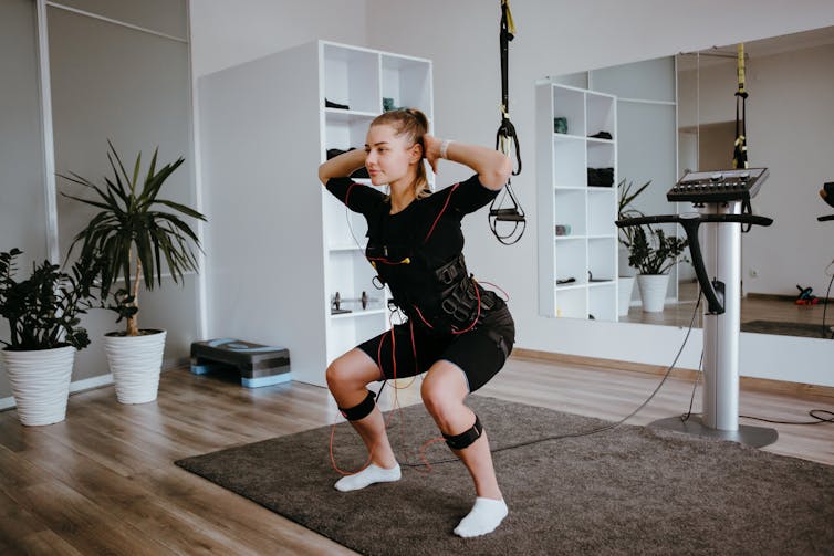 A woman performs a bodyweight squat while wearing an EMS suit.