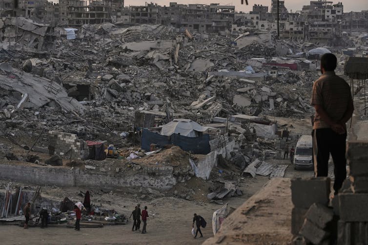people stand among the rubble of a destroyed residential area