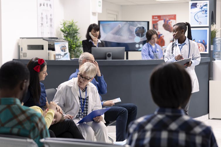 Busy health care waiting room with a doctor discussing treatment plans with mother and daughter and a desk in the background.