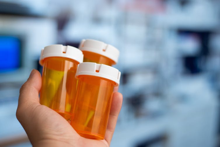 A person's hand holding three orange prescription medicines vials which are empty.