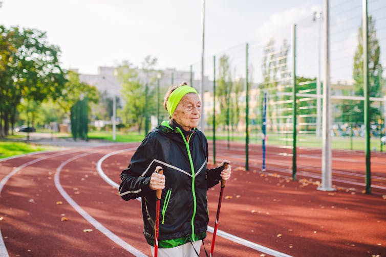 Elderly woman doing Nordic walking exercises with sticks outside in the city stadium