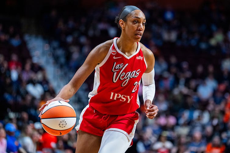 Young Black woman wearing a red jersey dribbles a basketball.
