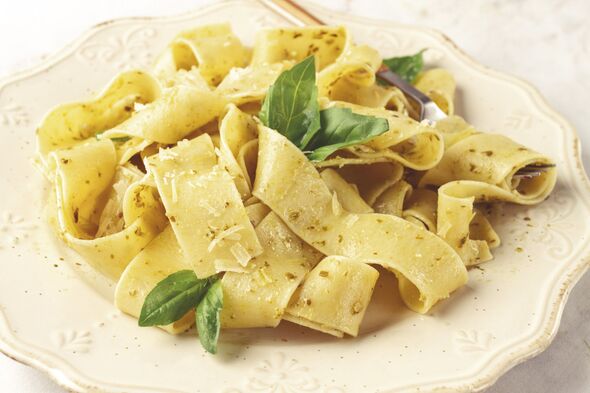 Fresh papardelle pasta, with basil and pesto sauce, is served, on a white plate, with a fork held by hand Fresh papardelle pasta, with basil and pesto sauce, is served, on a white plate, with a fork held by hand