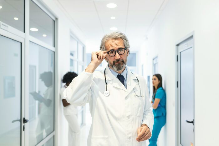 Senior doctor adjusting glasses in hospital corridor