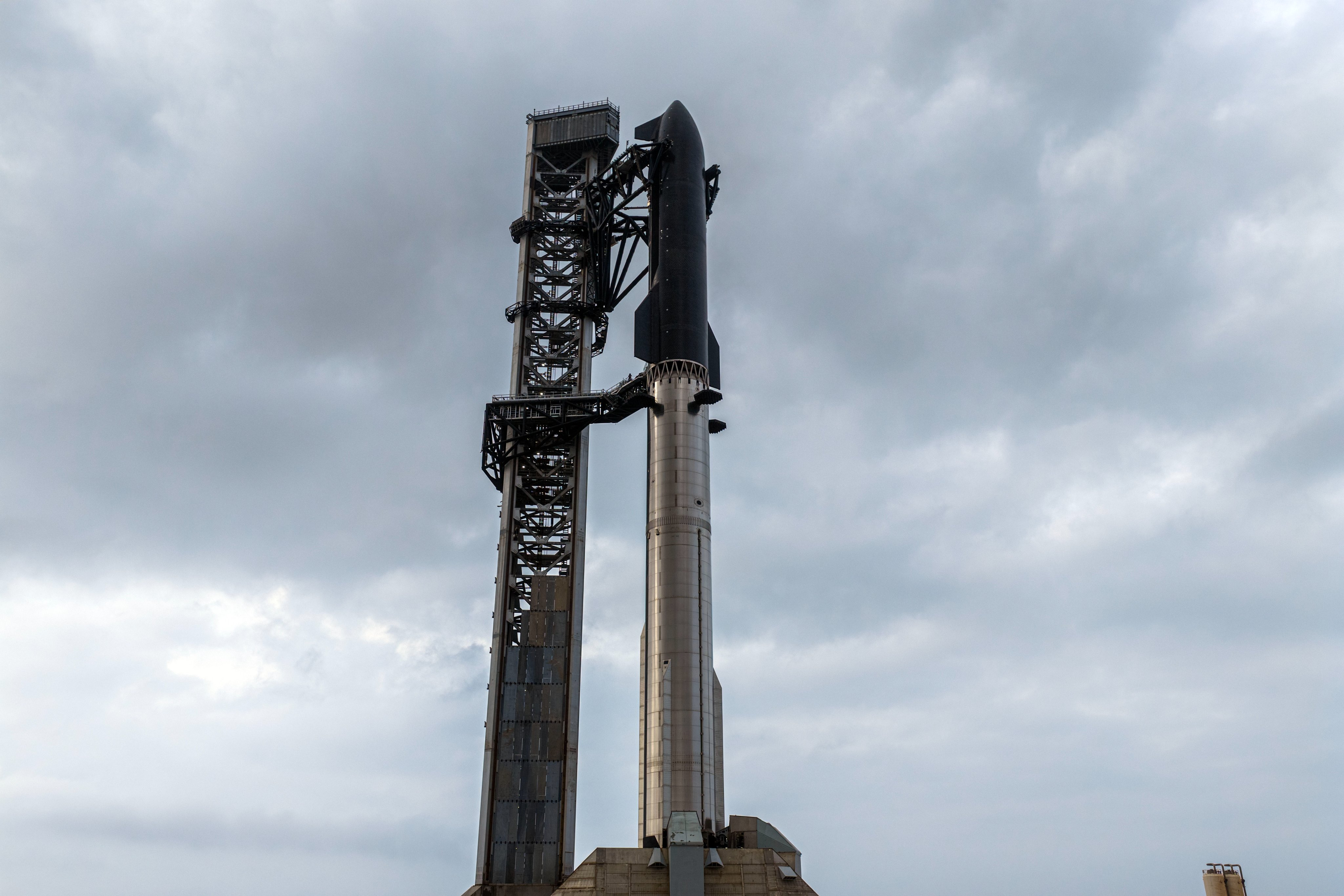 a giant chrome rocket booster and black-tiled spacecraft stand tall on a launchpad next to a gray tower.