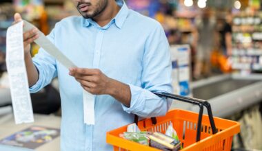 A man in a blue shirt examines a grocery receipt while holding an orange shopping basket in a supermarket.