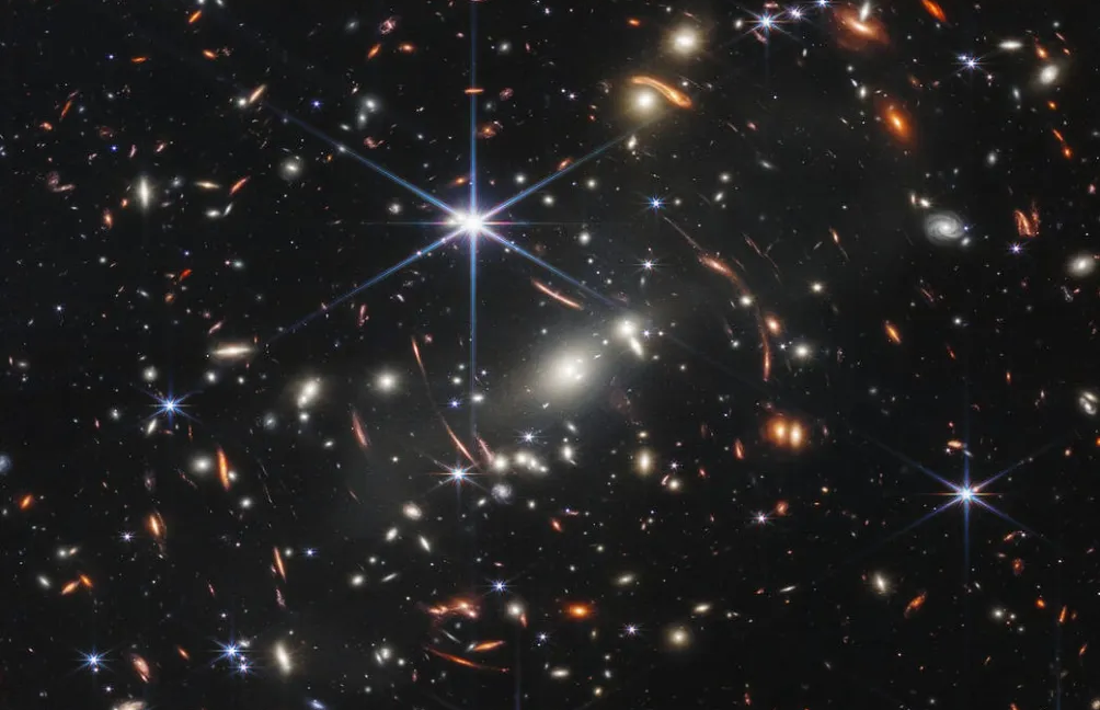 Image of a field of stars and galaxies, with most of them distorted by a gravitational lens.