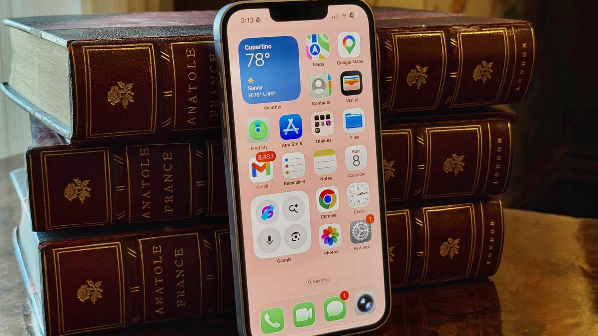 The iPhone 17E leans against leather-bound books