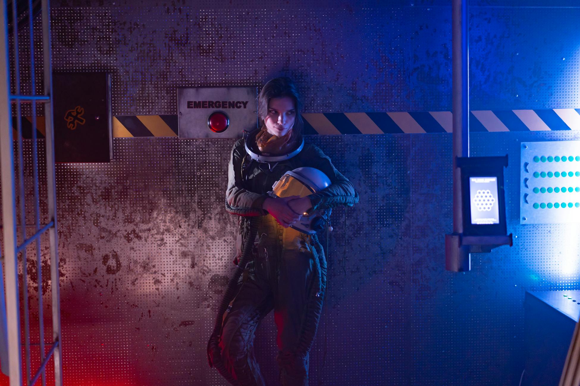 A woman in a spacesuit stands in a futuristic spaceship interior, illuminated by colorful neon lights.