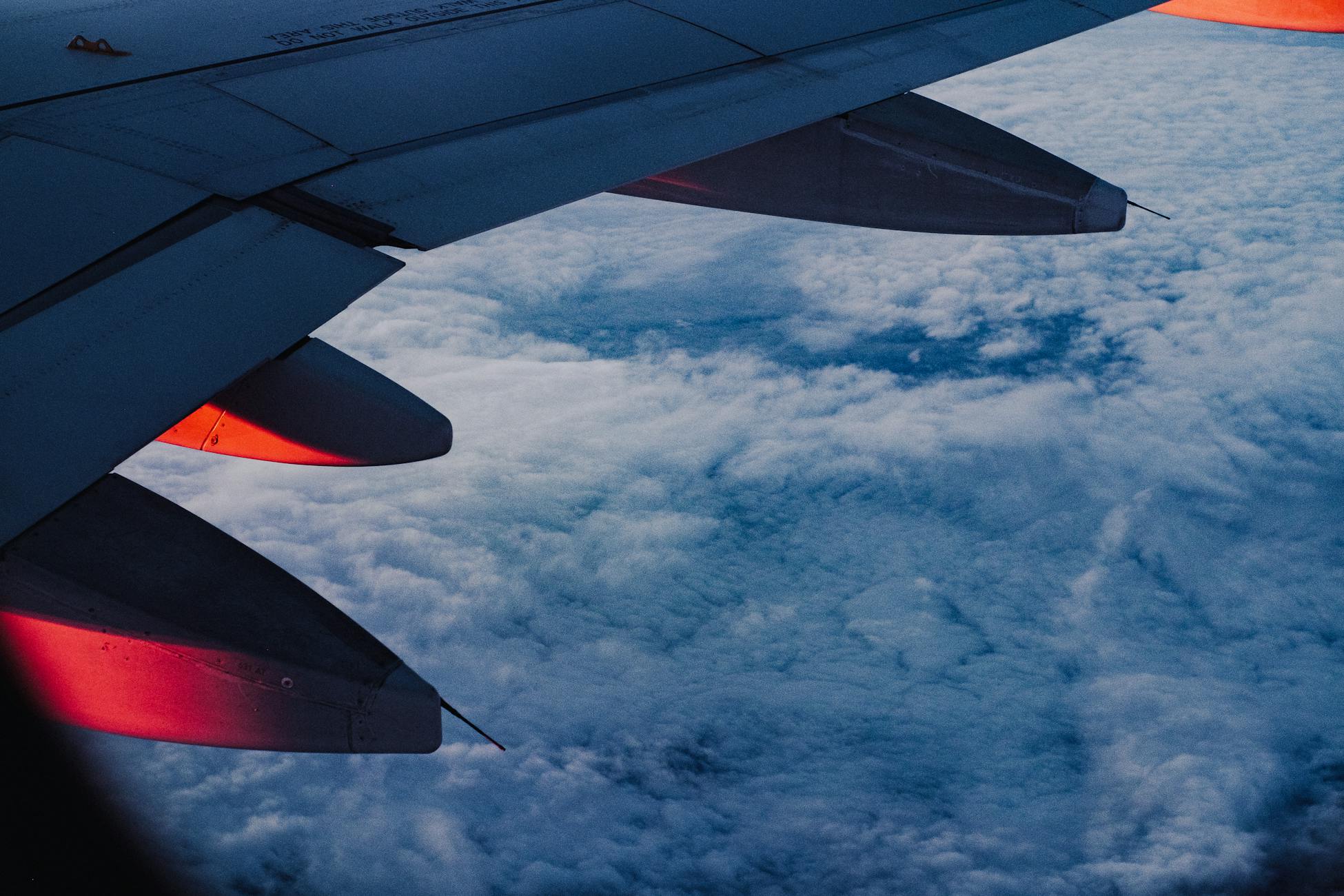 An airplane wing with dramatic lighting flying high over a sea of clouds during twilight.